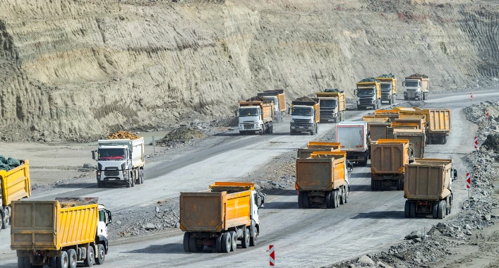 A line of haul trucks stuck or slowed on a deteriorated road, waiting to move