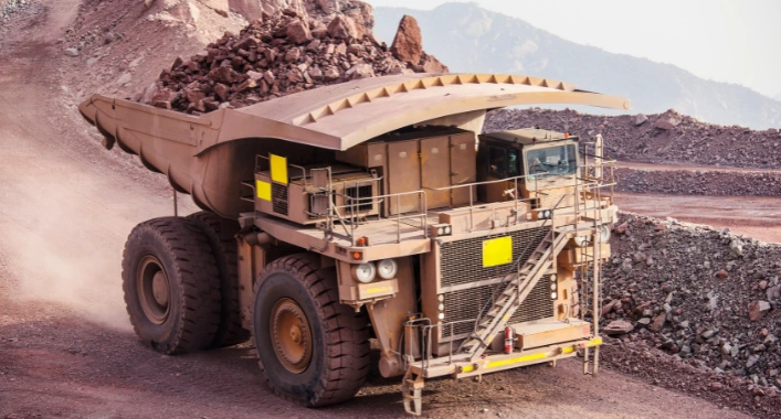 A mining truck navigating a sharp bend on a rough road with visible bumps and loose gravel, highlighting the risk